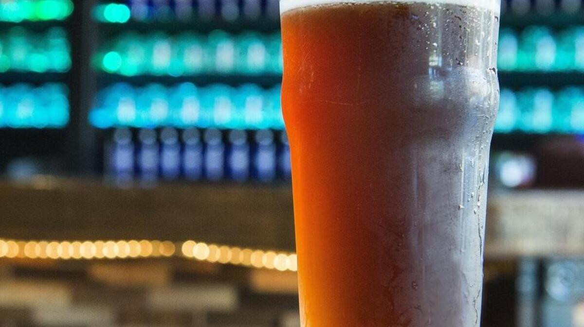 
A pint of Ottzel Quatzel sits on a table at Tacoma’s Odd Otter Brewing, with the bar’s glasses illuminated in their display behind the counter.
