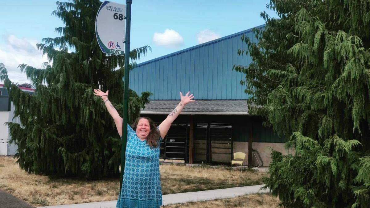 Olympic Cards and Comics’ owner Gabrielle Shephard Trautmann celebrates the new Intercity Transit bus stop with a July 25 photo.