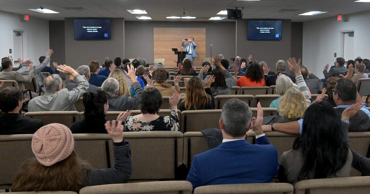 The congregation of the Olympia Kingdom Hall of Jehovah’s Witness wave en masse to fellow member Sean Grey as he takes a commemorative group photo after their reopening service and celebration on Jan. 15, 2023 after after a 2018 arson fire. The fire gutted the original hall on July 3, 2018 after suffering an earlier attack on March 19 of that year.. Both incidents were part of a string of eight known attacks that also affected Jehovah’s Witnesses properties in Yelm, Lacey, Puyallup and Shelton. an attack on March 19, 2018.