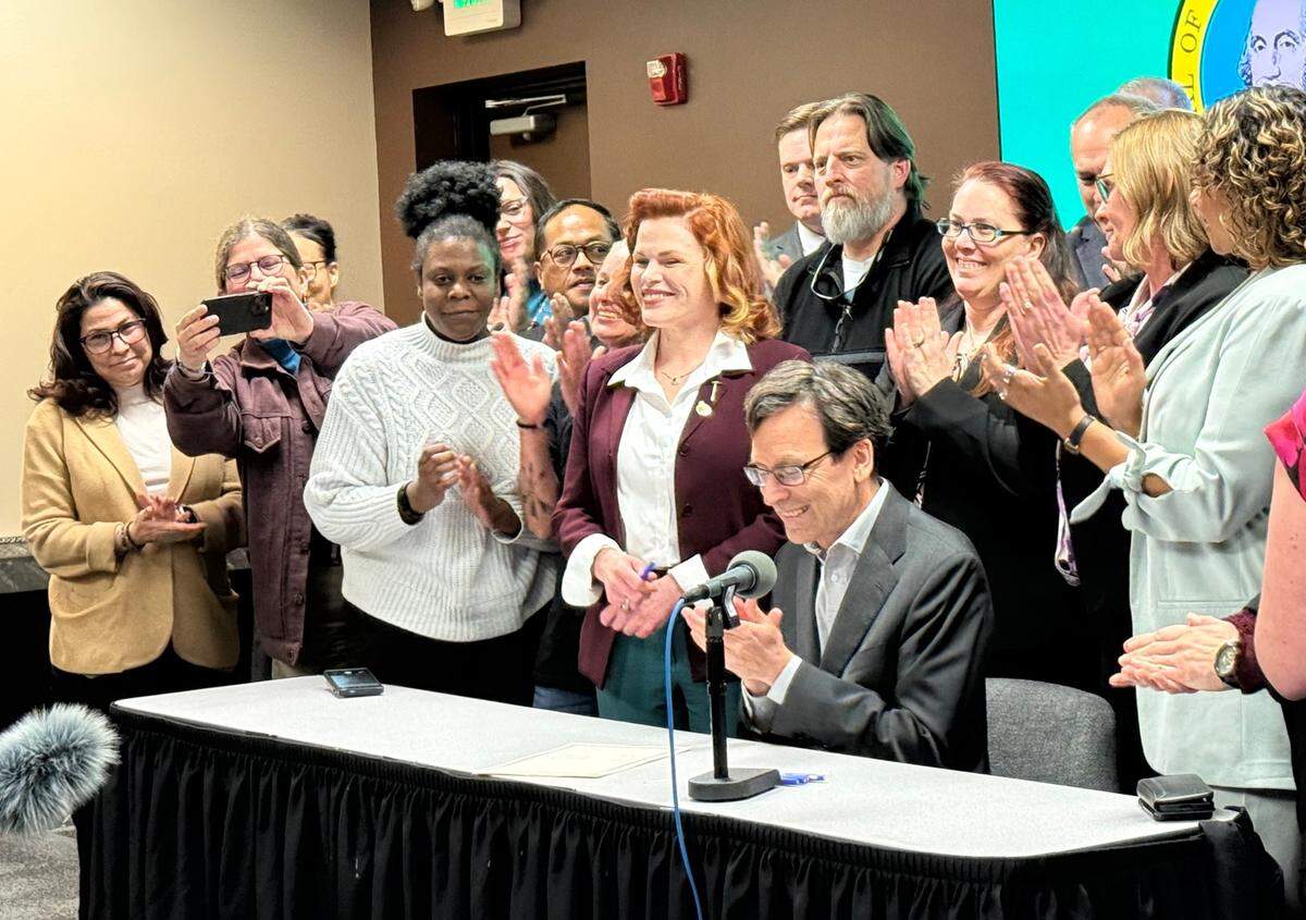 State Rep. Mary Fosse (center) and Gov. Bob Ferguson (seated) smile during the signing of House Bill 1644 on Monday, April 28, 2025.