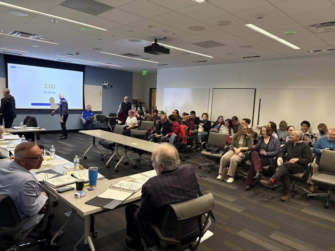 South Puget Sound Community College President Timothy Stokes speaks to Trustee Steven Drew in the foreground as the room fills for Tuesday’s Board of Trustees meeting.