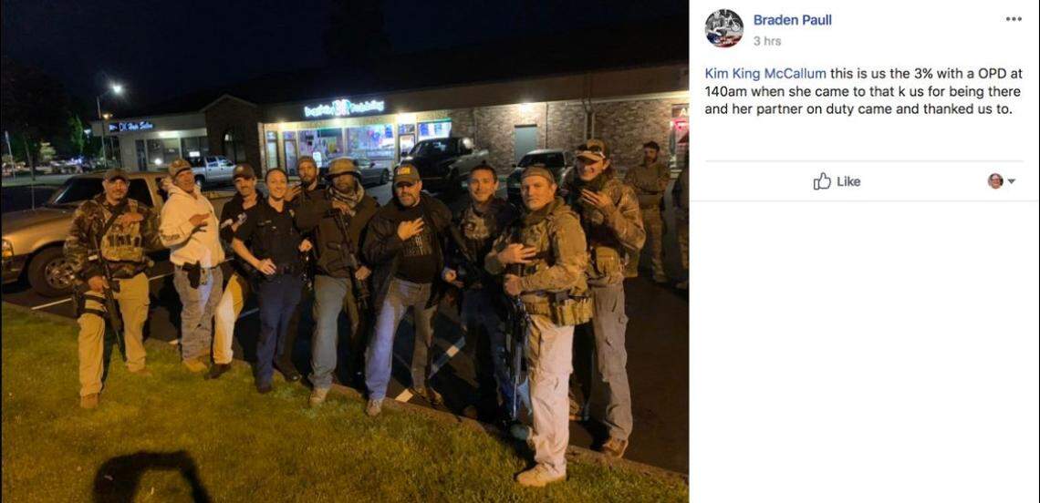 A photo posted on Facebook shows an Olympia Police officer posing with a group of armed men flashing hand gestures associated with The Three Percenters movement.