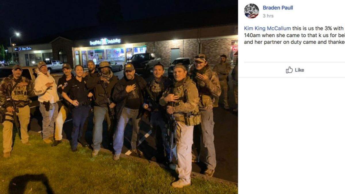 A photo posted on Facebook shows an Olympia Police officer posing with a group of armed men flashing hand gestures associated with The Three Percenters movement.