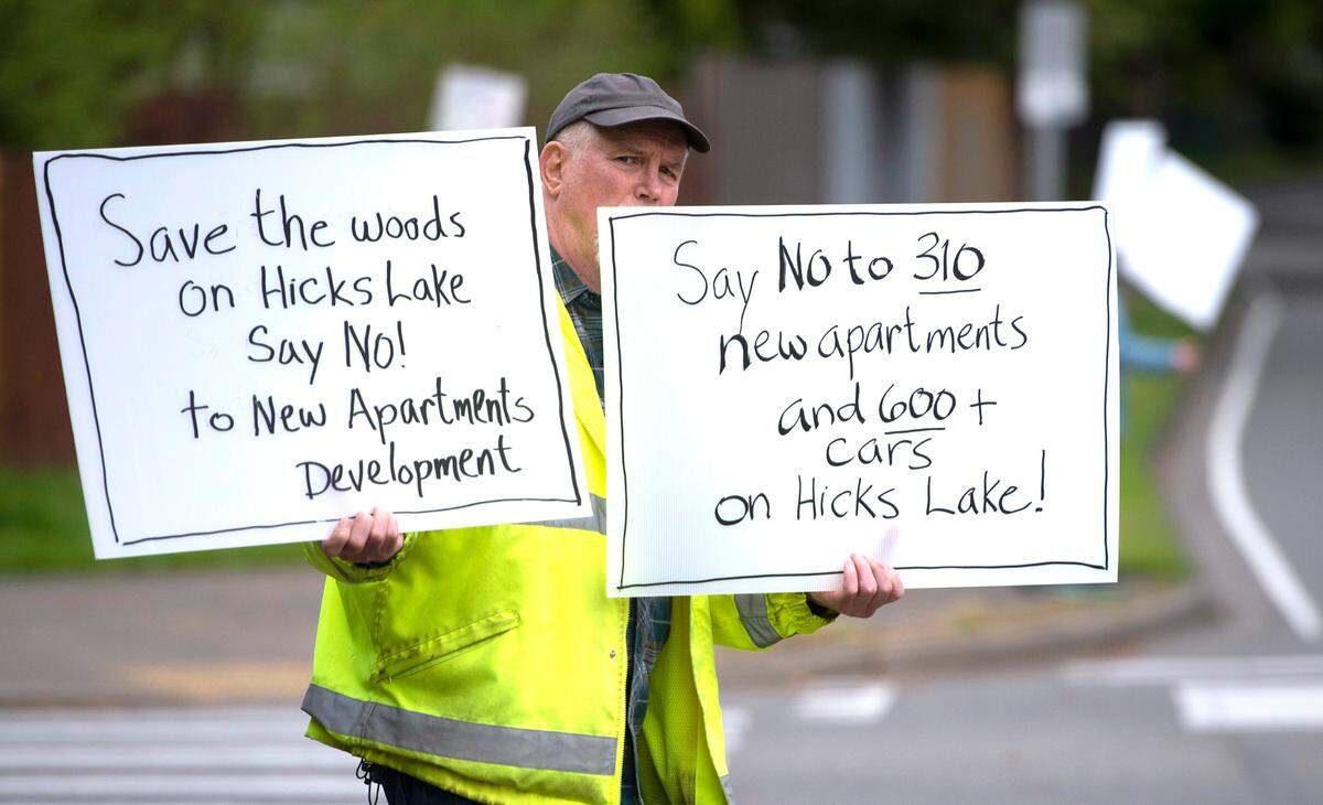 Vern Dearing holds signs as he joins neighbors to protest the proposed apartment complex in their Hicks Lake neighborhood along Ruddell Road in Lacey, Washington, on Friday, May 13, 2022.