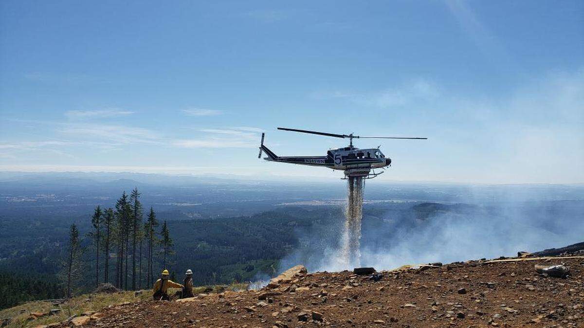 A Department of Natural Resources helicopter dumps water on a fire in the Capitol State Forest to slow it’s spread.
