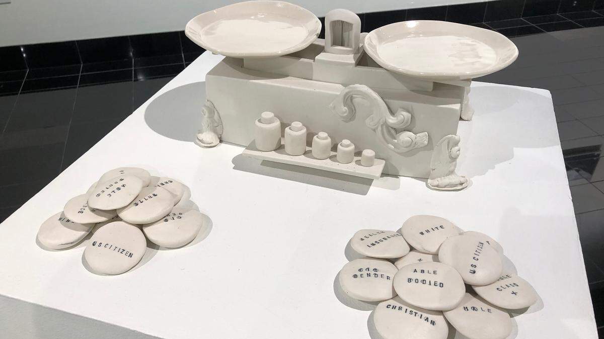 The ceramic Weight of Privilege Game, created by studio technician and teacher Nicole Gugliotti in collaboration with fellow artist Mac McCusker of Durham, N.C., includes scales and game pieces labeled with privileged statuses.