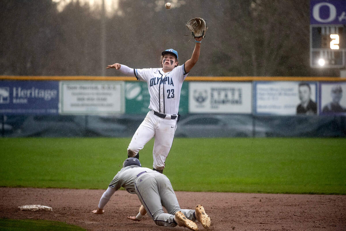 Olympia shortstop Trace Pruitt leaps to corral a high throw as Puyallup’s Cameron Hale slides safely into second base during Wednesday afternoon’s baseball game at Olympia High School in Olympia, Washington, on April 12, 2023. Puyallup won the game, 6-2.