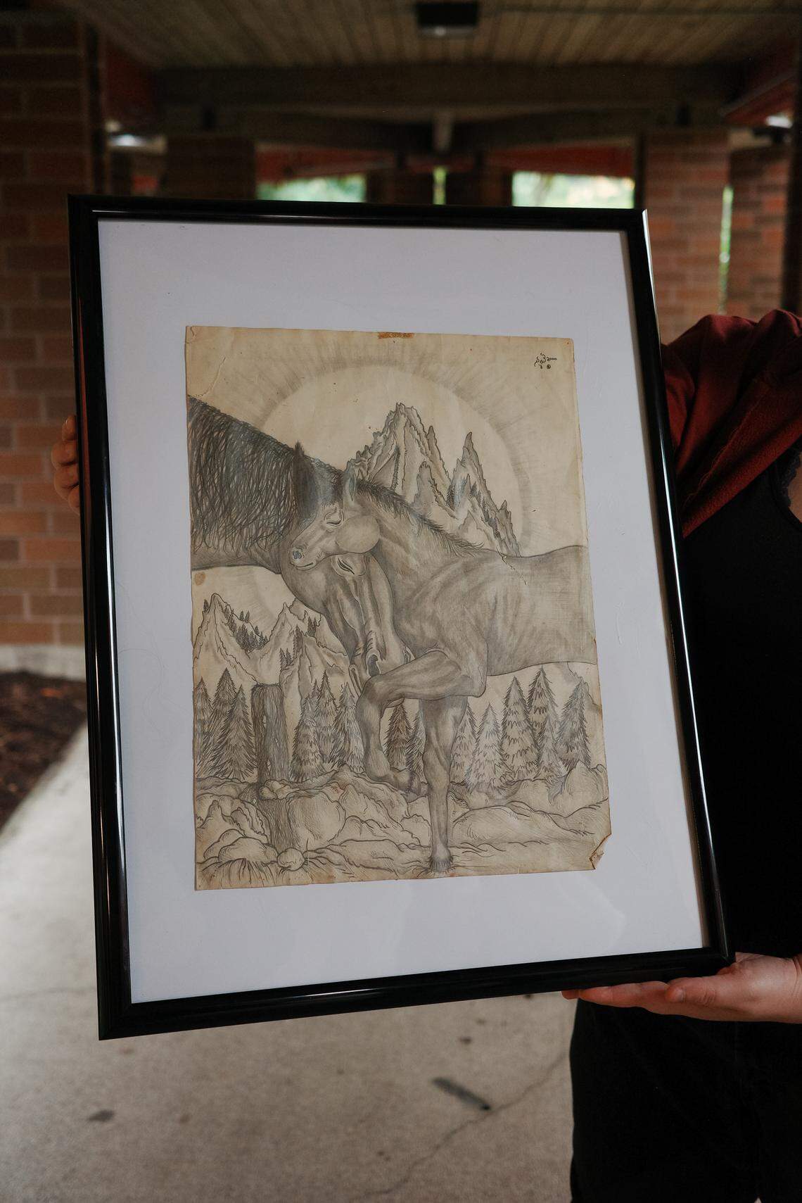 Mariah Schoening, 23, holds up a drawing of horses created by her father Zebediah Starbrow Schoening, 47. Schoening died on Oct. 25, 2024, a few weeks after being set on fire near his tent at “The Jungle” homeless encampment on Martin Way East in Olympia. Two defendants have been sentenced in connection to her father’s death.