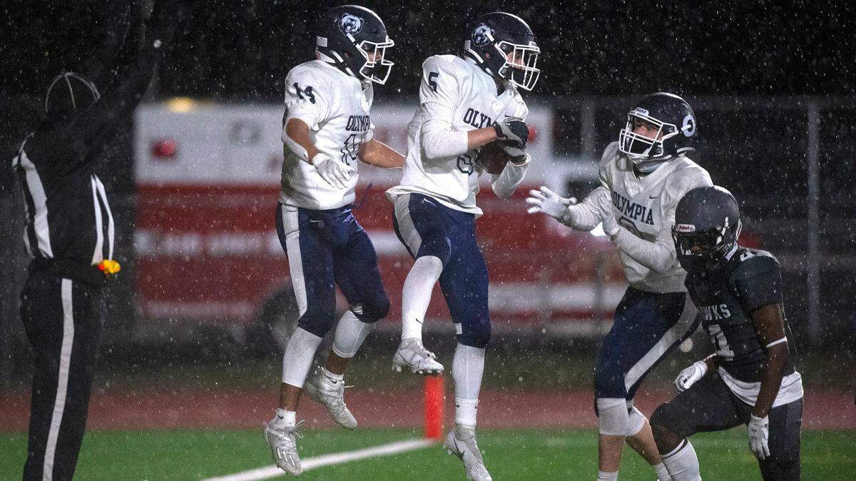 Olympia’s Alfredo Ramirez-Cortes (from left), Mason Juergens and Jack Olsen celebrate Juergens’ touchdown reception in front of River Ridge defensive back Dorian Cotton during Friday night’s high school football game at South Sound Stadium in Lacey on Friday, March 19, 2021.