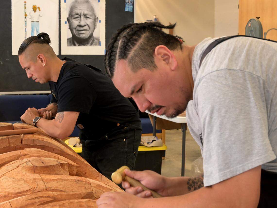 With the image of Billy Frank Jr. watching over them, Ablaza Pluff and Earl Pluff continue their carving of the 13-foot story pole honoring him and other Indigenous activists in the Pay3q’ali carving studio during a June 25 work session on the Indigenous Arts Campus at The Evergreen State College in Olympia. The project is part of a six-month residency hosted by the Longhouse Education and Cultural Center.