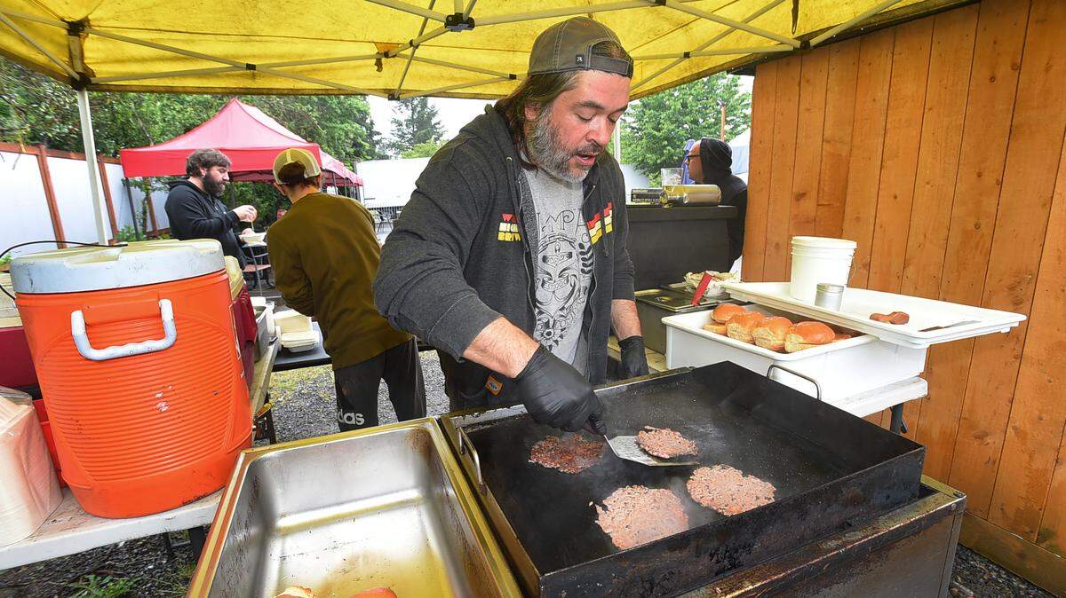Patrick Jansen serves up four burgers at Carbon Pop’s pop-up food stand as assistant Ryder White takes another order outside Northwest Beerkworks in Olympia on Thursday, June 9, 2022.