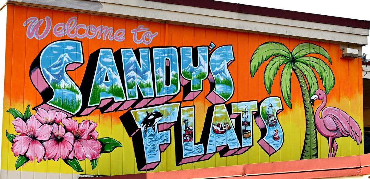 Keith Henderson, a Portland-based artist, created a colorful overhead mural​ honoring Sandy Betz, the namesake of the apartment complex. The name “Sandy’s Flats” honors Sandy Betz, a former housing guest who was well recognized in and around the Olympia community. The colorful overhead mural bearing her name was created by Keith Henderson, a Portland-based artist.
