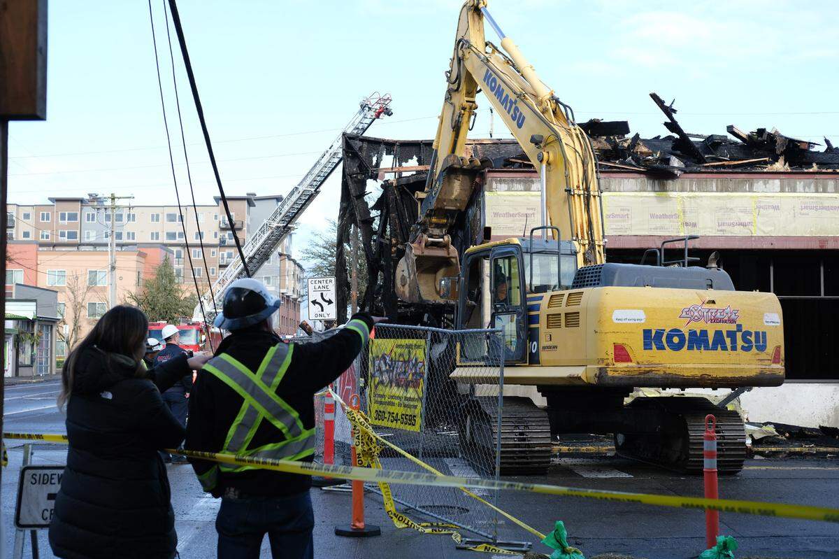 A large yellow excavator started to sift through debris on the edges of the charred apartment building at 310 Capitol Way North, Olympia on Thursday, Dec. 16, 2021. Kevin Bossard, assistant chief of operations with the Olympia Fire Department, said the investigation remains in its early stages and the excavator was on standby.
