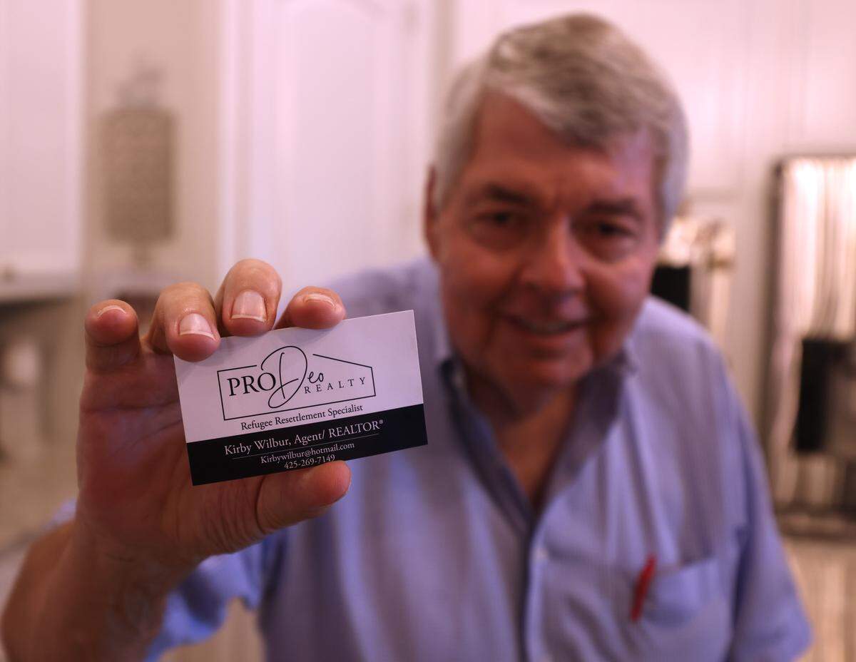 Kirby Wilbur shows off his business card at his home in McKinney, Texas, Monday, May, 18, 2026. The tag line from his card reads “Refugee Resettlement Specialist.” He has helped several Seattle/Tacoma area families relocate to Texas.