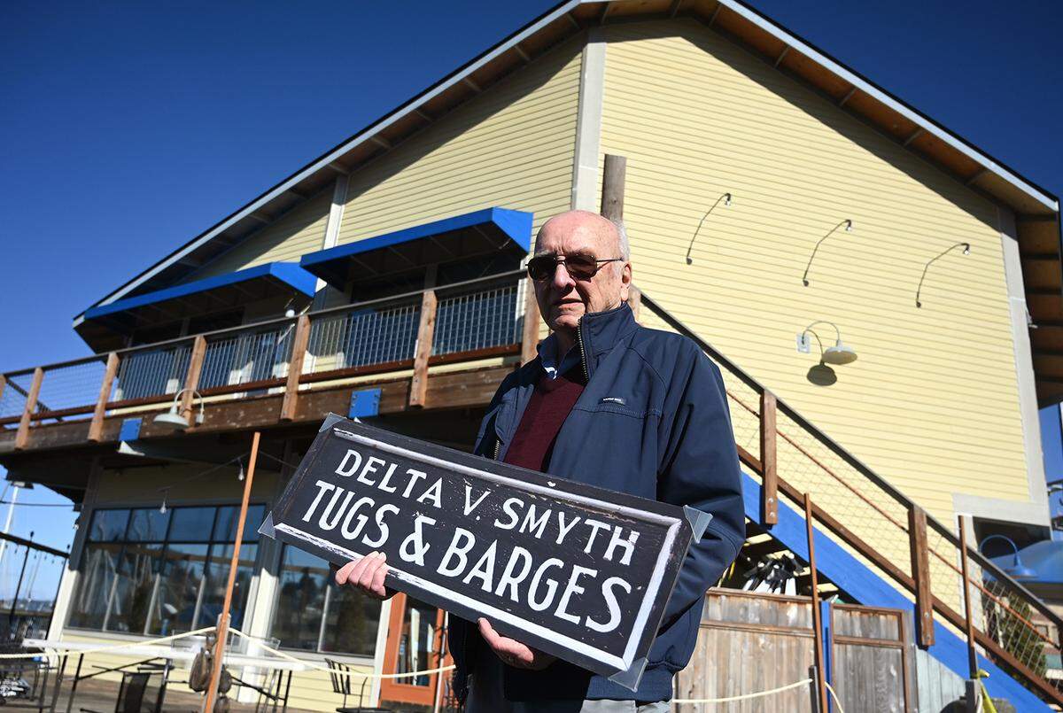 Standing in front of the Budd Bay Cafe, Chuck Fowler, past president of the South Sound Maritime Heritage Association, holds the original business sign for the Delta V. Smyth Tugs & Barges company which was located at the same site of the current restaurant along Percival Landing in Olympia. The sign will be on display with other historic pieces for public viewing after the restaurant reopens March 1.
