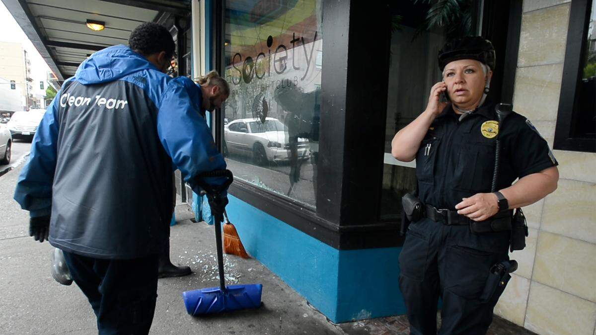 Olympia police Sgt. Amy King responds to a broken window at the Society Bar & Nightclub along Fourth Avenue East Wednesday morning as two members of the city’s Clean Team sweep up.