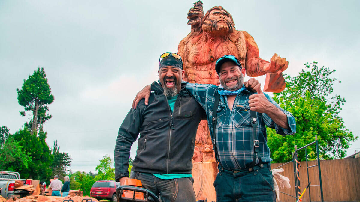 Tony Robinson and Bernie Madison pose for a photo in front of the 17-foot Sasquatch carved with chainsaws and now on display in downtown Oakville.