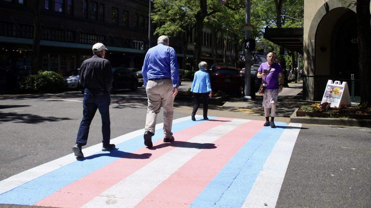 People walk on the crosswalks at Washington and Fifth Avenue in downtown Olympia on Saturday, June 3, 2023. City officials led a commemoration event for Pride Month and the crosswalks painted the colors of the transgender flag.