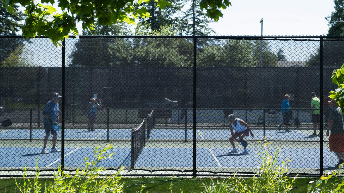 A pickleball player crouches to hit a ball as it travels past a net on a Woodruff Park pickleball court in west Olympia on Friday, May 31.