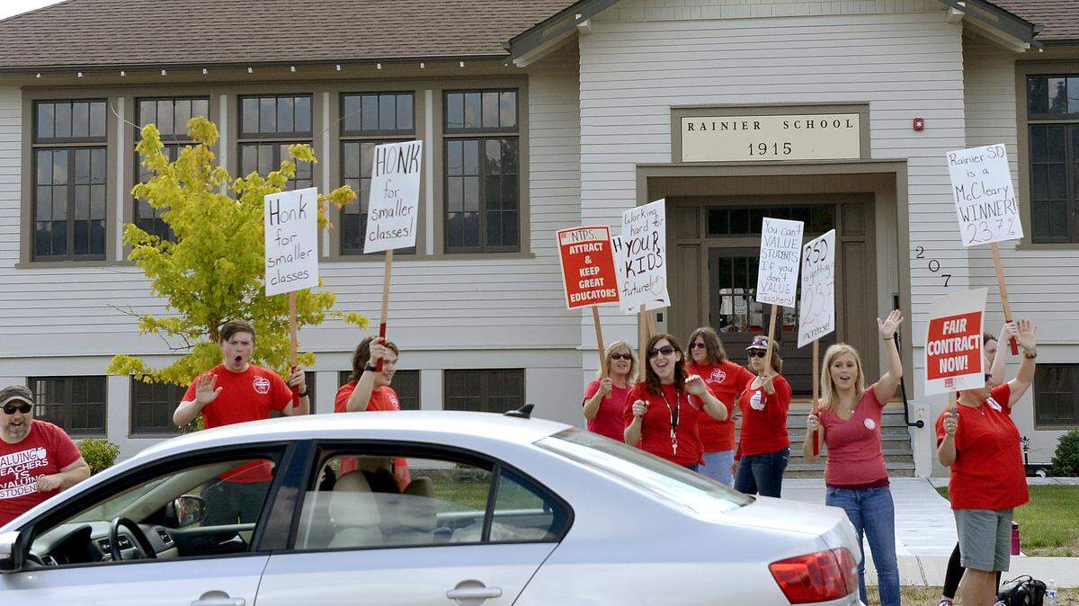 Teachers and their supporters waive signs along Centre Street in Rainier on Monday. The district now says it has a tentative contract agreement with the Rainier Education Association and that school will start Thursday.