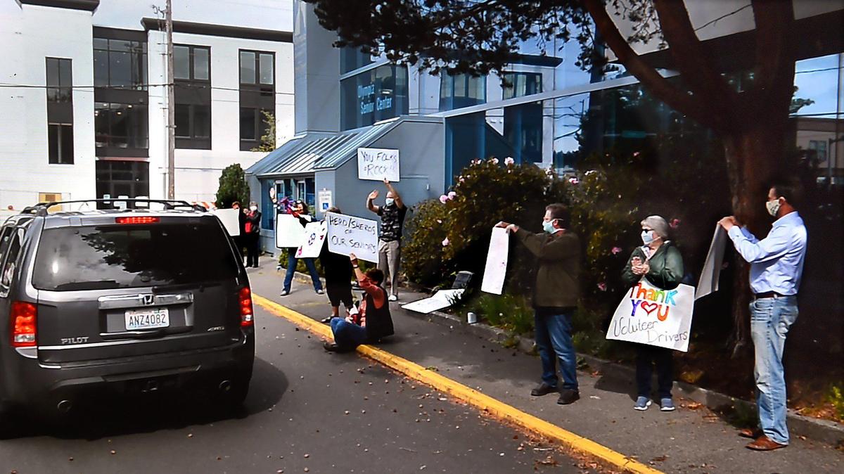 Board members and supporters for Senior Services for South Sound join executive director Brian Windrope to wave signs of thanks to Meals on Wheels drivers as they pick up food for their delivery runs from The Olympia Center.