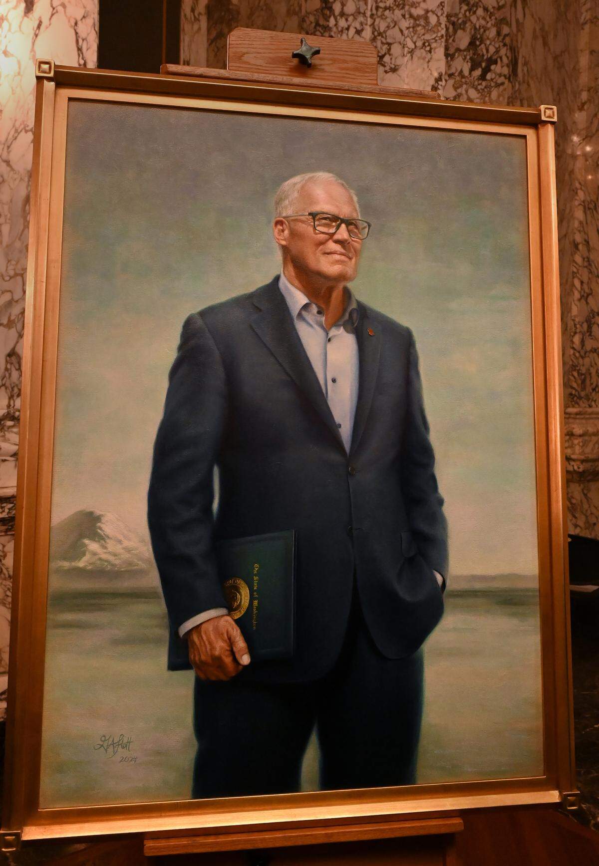 Gov. Jay Inslee — and his environmentalist spirit — have been immortalized in an official portrait. In the painting Inslee stands with an expression that reads equal parts determination and hope. He casts his gaze slightly upward, with his left hand in his pocket and right hand holding an evergreen-colored folder emblazoned with the state seal.