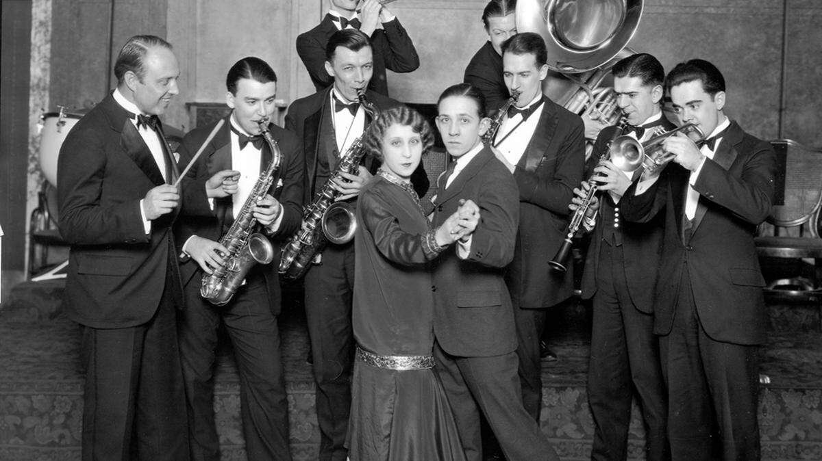 Charleston contestants and the orchestra at Tacoma’s Winthrop Hotel. The jazz band stands behind the couple, instruments raised, as if playing.