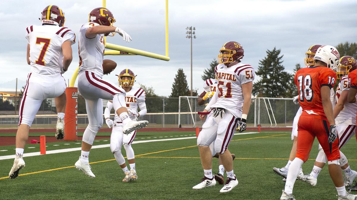 Capital players celebrate Chris Penner’s (second from left) touchdown catch over Lakes defensive back Philip Riley (18) during Friday night’s season-opening football game at Harry E. Lang Stadium in Lakewood on Aug. 31, 2018.