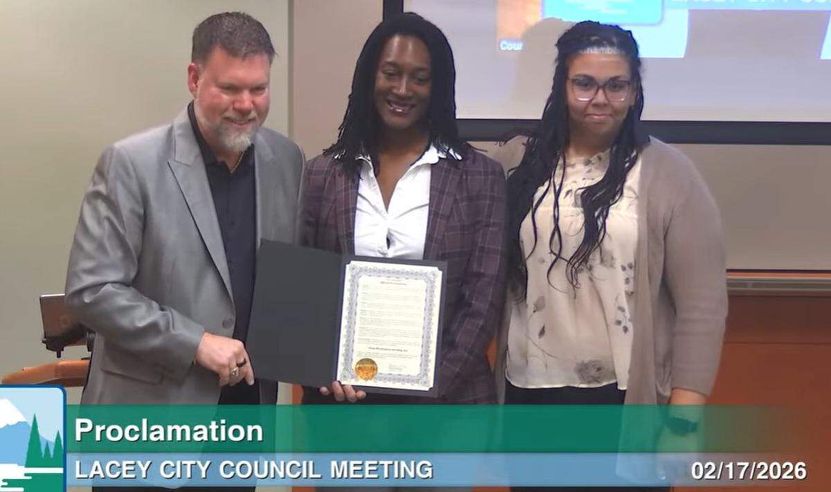 Washington state Office of Equity Director Megan Matthews (center) accepts a proclamation from Lacey Mayor Andy Ryder during Tuesday’s Lacey City Council meeting on Feb. 17, 2026.
