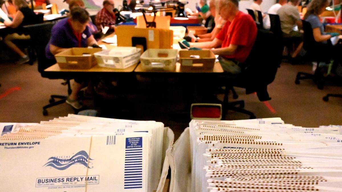 Primary ballots are shown in the foreground during a busy day at the Thurston County ballot processing center.