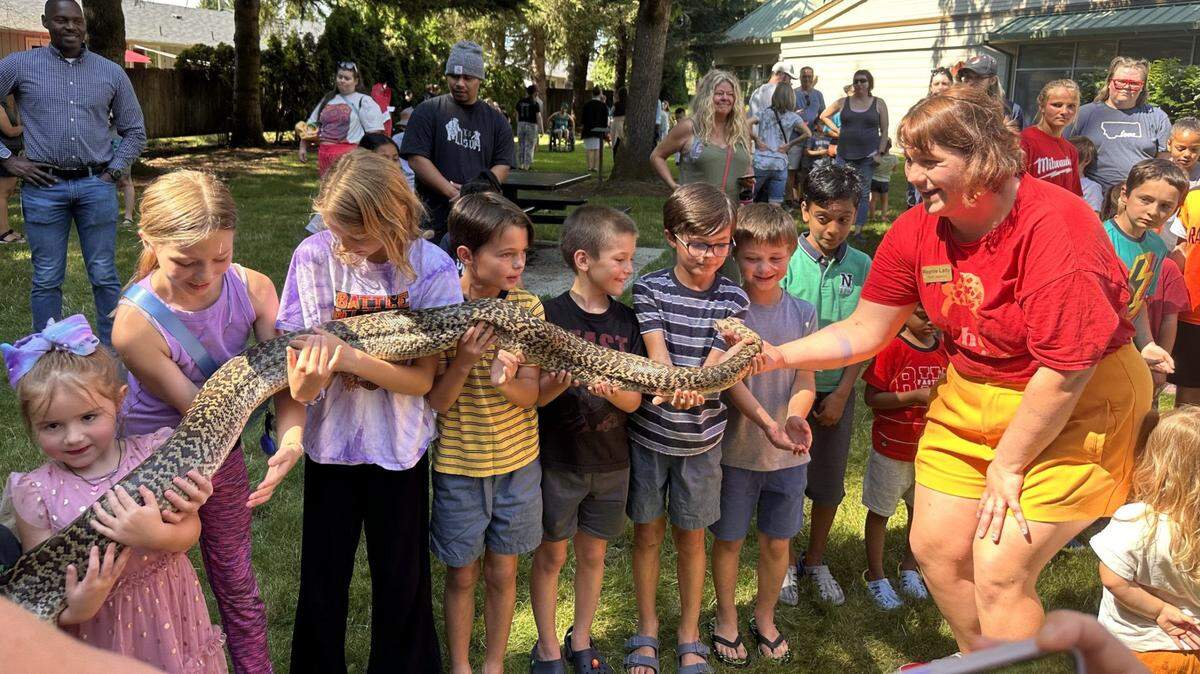 Reptile Lady helps kids standing in a row to hold up a long snake together