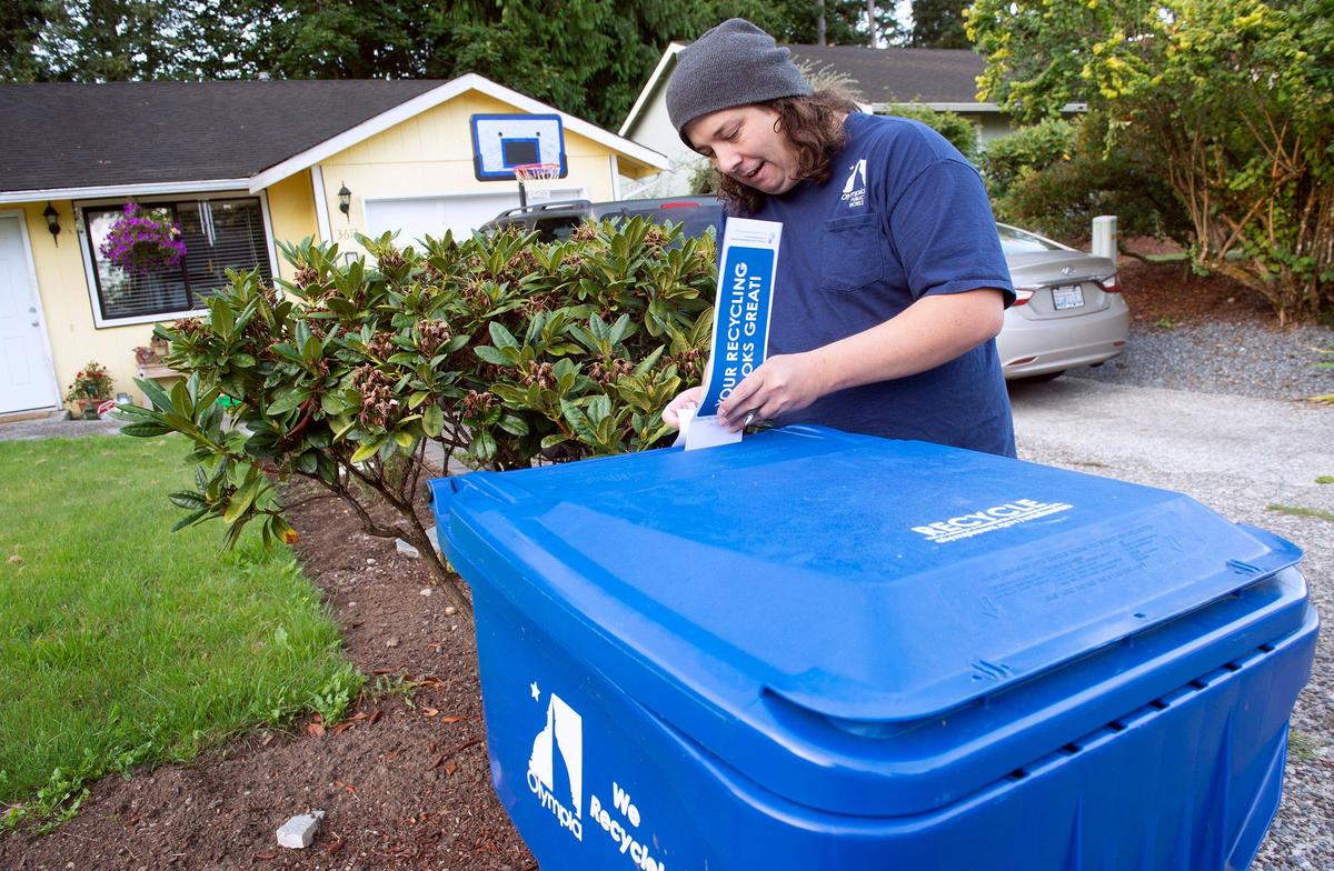 City of Olympia intern David Stocks puts an informational placard on a recycling bin along Autumnwood Court in an southeast Olympia.