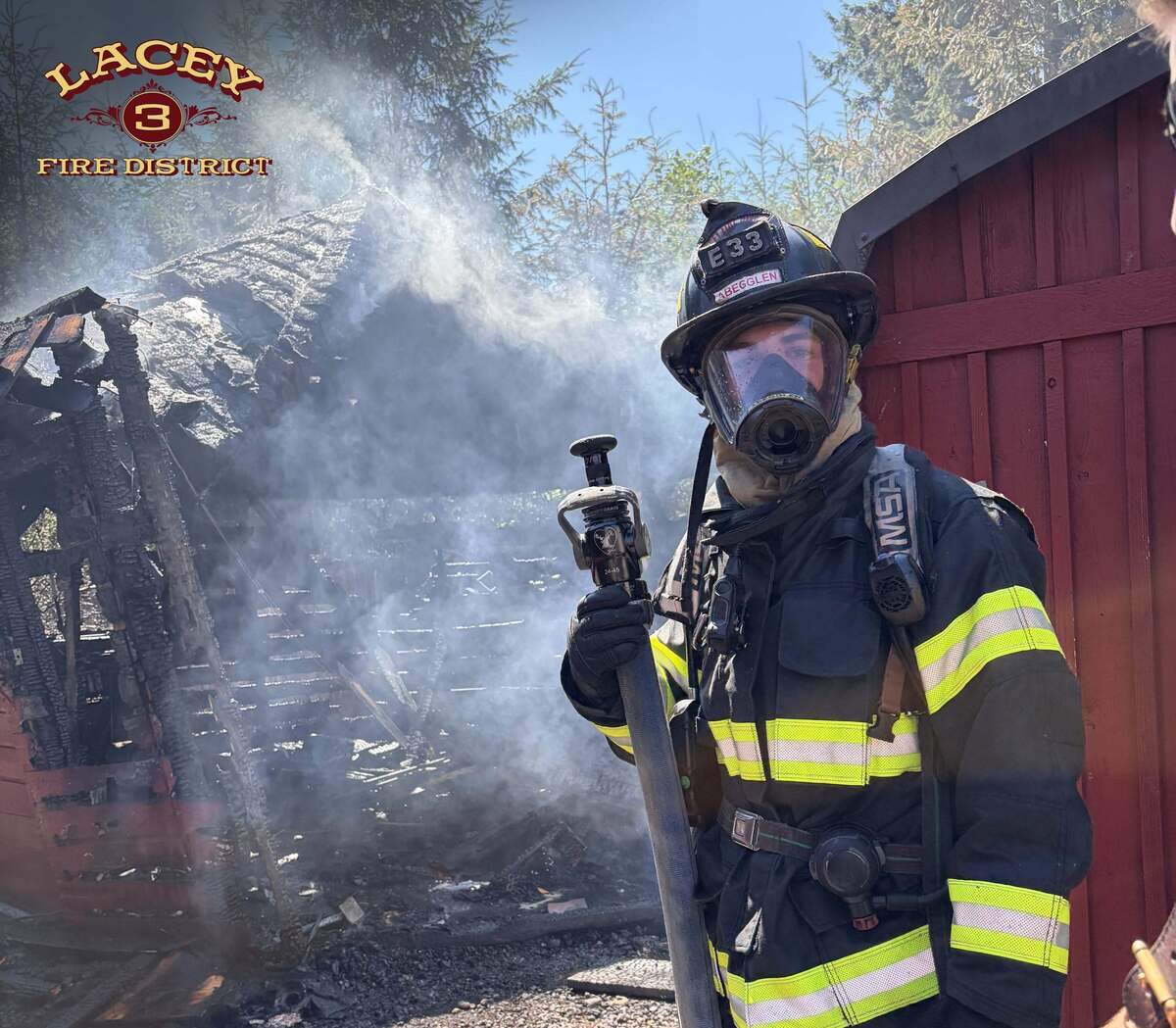 A Lacey Fire District 3 firefighter stands in front of a large shed near the 3600 block of Carpenter Road Southeast that was destroyed in a fire on Monday, July 6, 2026.