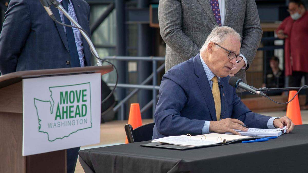 Gov. Jay Inslee signs into law climate legislation including a 16-year $17 billion transportation package in front of the Tacoma Dome Station on Friday. Rep. Jake Fey, D-Tacoma, and Sen. Marko Liias, D-Lynnwood, who sponsored some of the legislation, stood behind the governor.