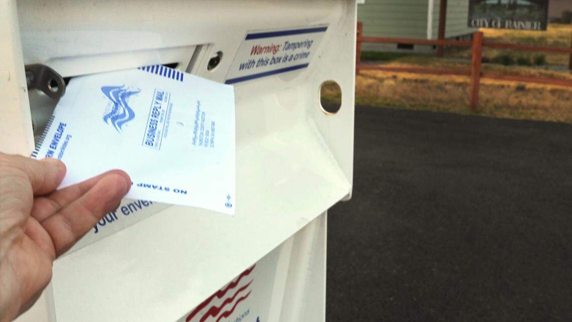 A voter places their ballot in a dropbox near Rainier City Hall.