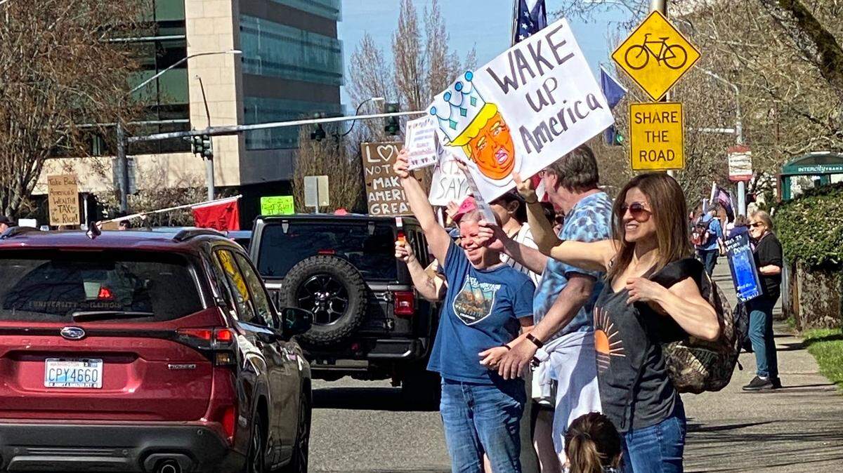 People wave signs along Capitol Way on the Capitol Campus in Olympia on April 5, 2025. More than 5,000 people came out to rally against President Trump’s cuts and policies.