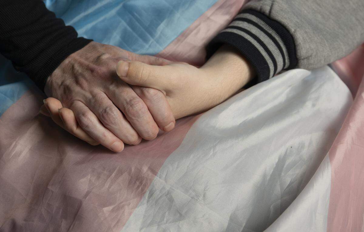 Melinda Ramirez and her son, Vincent, hold hands over a transgender pride flag in their apartment on January 14, 2026, in Seattle, Wash. The pair moved to Seattle from Houston in December 2024, in the wake of Texas’ ban on gender-affirming healthcare.