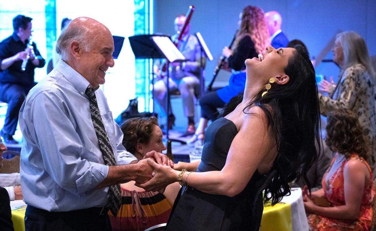 Alexandra Arrieche laughs with first violin player Dan Szekely of Steilacoom after being announced as the new music director for the Olympia Symphony Orchestra during their fundraising gala at Indian Summer Golf & Country Club in Olympia, Washington on Friday, June 24, 2022.