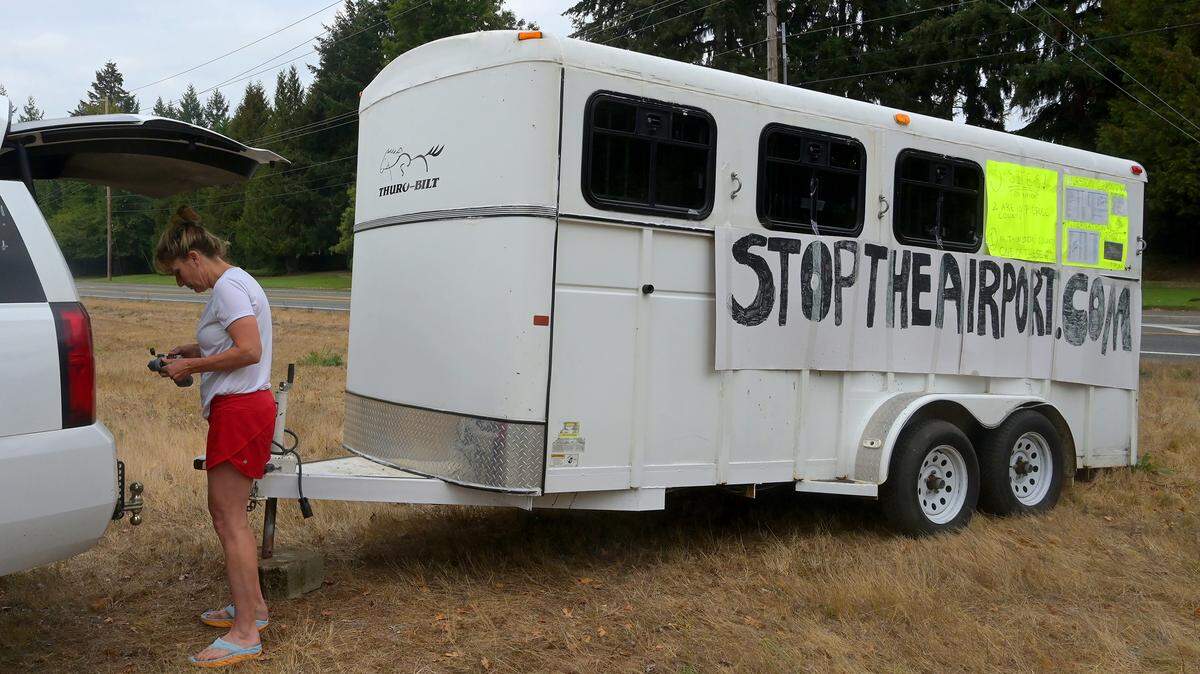 Amanda Sanders, a Thurston County resident, stands by a large horse trailer with signage protesting a proposed Thurston County airport on on Monday, Oct. 17, 2022. Sanders parked the trailer by the intersection of Yelm Highway Southeast and Spurgeon Creek Road near Pattison Lake.