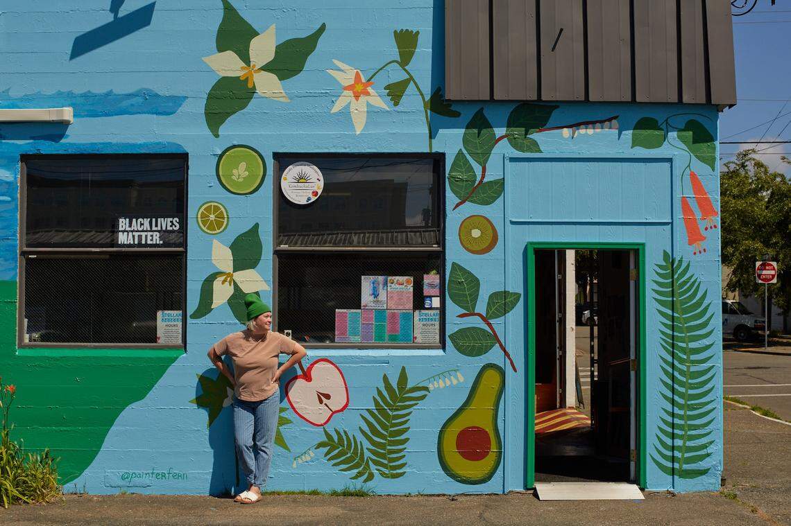 Fern Tallos poses with a mural she painted at the now-closed Stellar Juices, 623 5th Ave SE, Olympia.