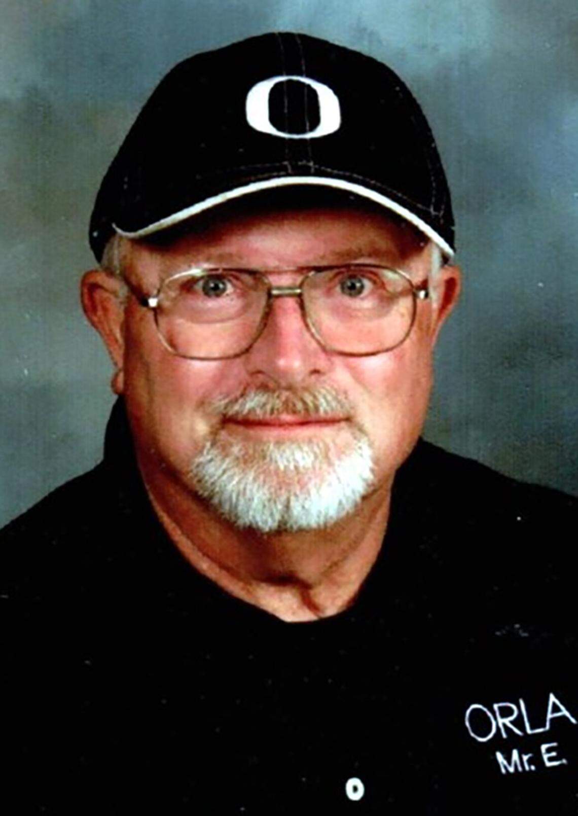 Randall "Randy" Edwards poses for a photo in front of a blue background. He is wearing a black hat and shirt.