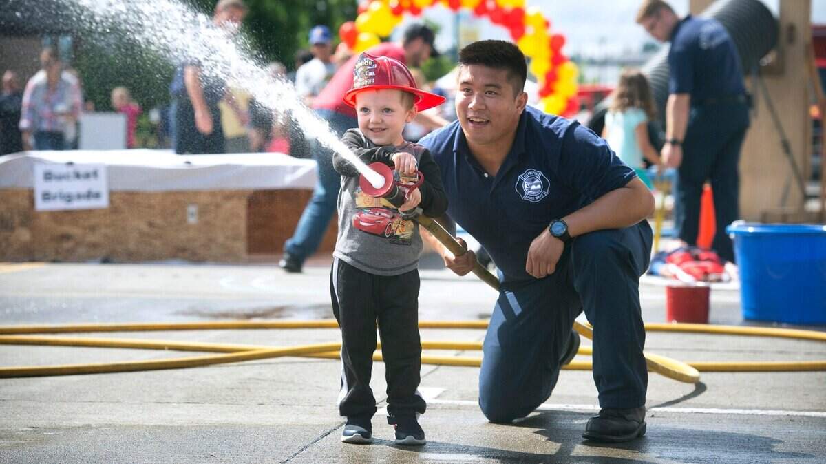 Olympia firefighter Julian Dizon assists Silas Johnson, 4, as he hoses down a “house fire” as he runs through the firefighter obstacle course during the Fire Rescue Spectacular event at the Hands On Children’s Museum in downtown Olympia on Saturday, June 23, 2018. 