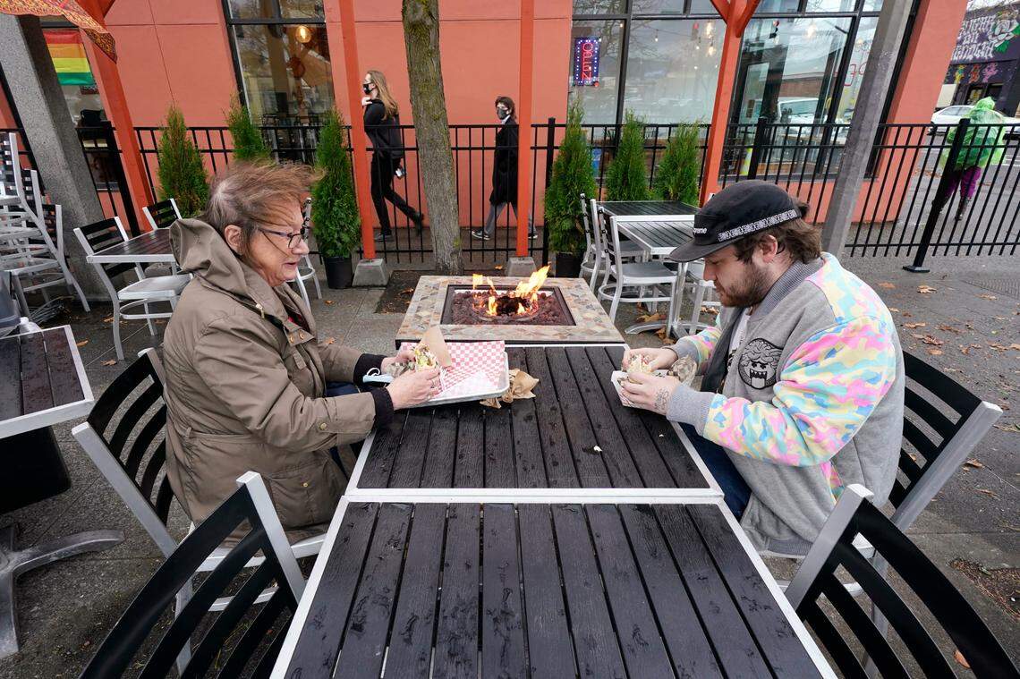 Diners Bonnie Breitman, left, and Casey McGan huddle near an outdoor gas fire as they eat lunch outside in a blustery wind Tuesday, Nov. 17, in Bellingham. Washington Gov. Jay Inslee on Sunday, Nov. 15, announced tighter restrictions in the state in response to a flood of new cases of COVID-19, the disease caused by the coronavirus. On Friday. Nov. 20, Inslee announced a $135 million economic relief package meant to support businesses and workers impacted by the latest round of restrictions introduced as the state experiences a surge in COVID-19 cases.
