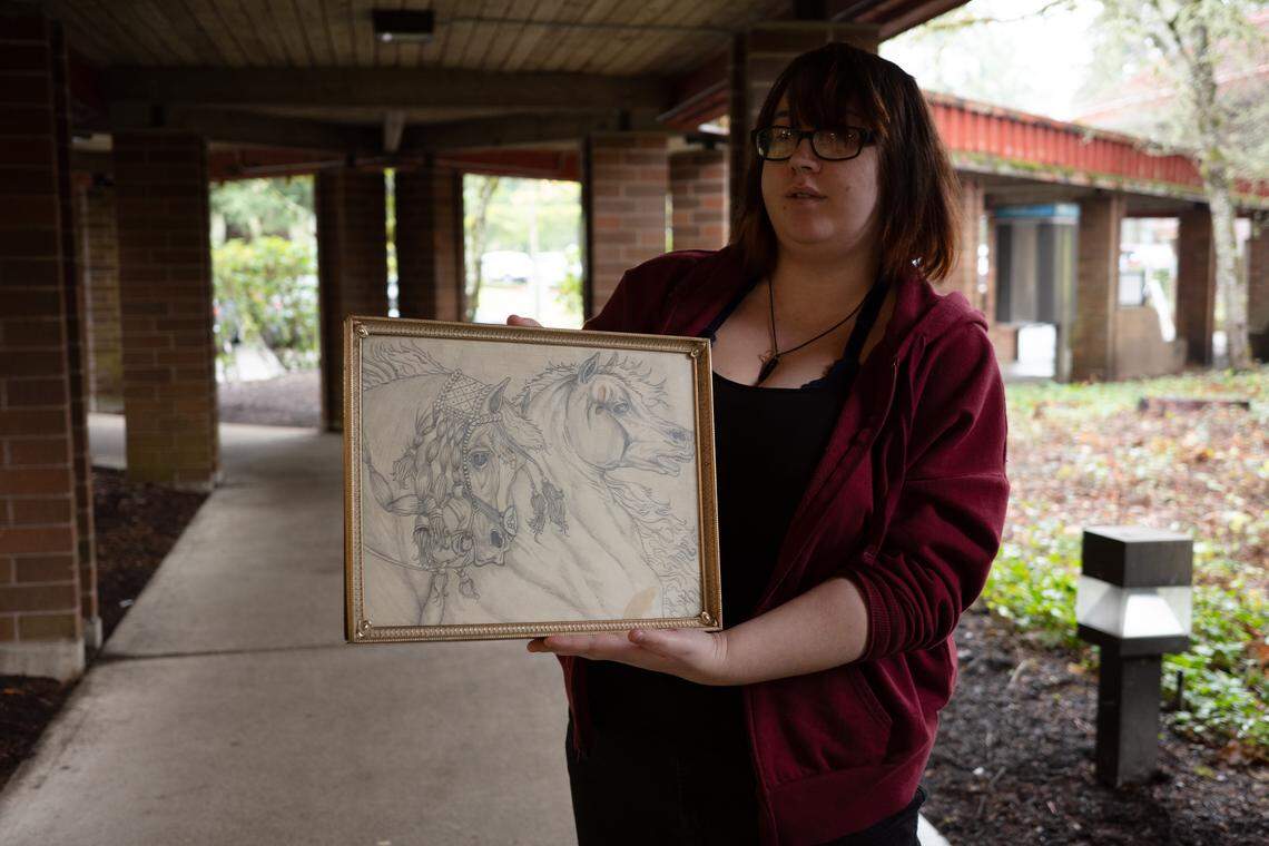 Mariah Schoening, 23, holds up a drawing of horses created by her father Zebediah Starbrow Schoening, 47. Schoening died on Oct. 25, 2024, a few weeks after being set on fire near his tent at “The Jungle” homeless encampment on Martin Way East in Olympia. Two defendants have been sentenced in connection to her father’s death.