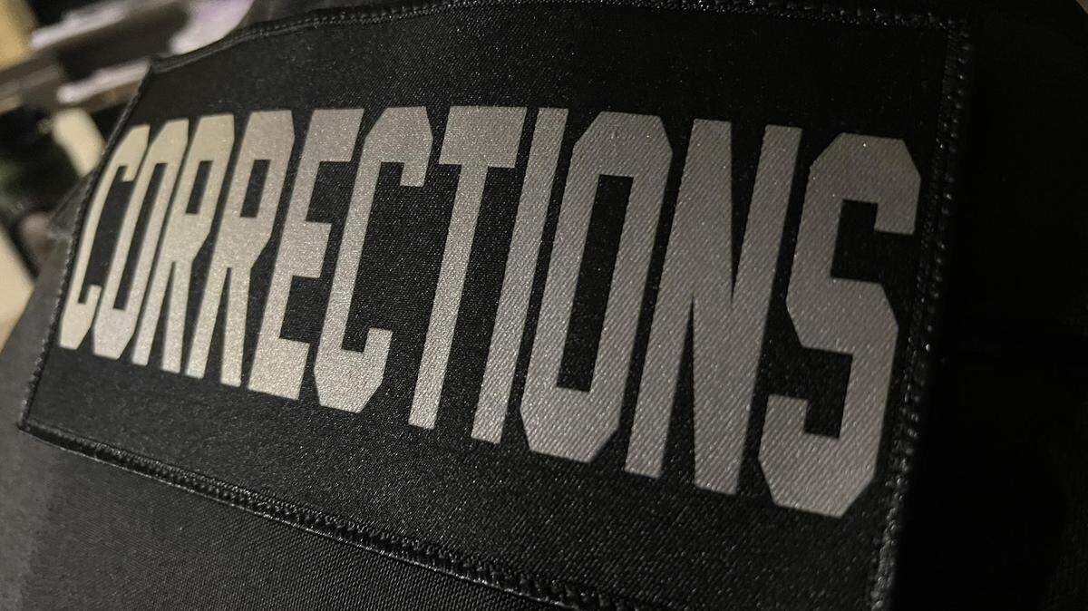 The word "corrections" in grey letters on a black background on a correctional officer's uniform