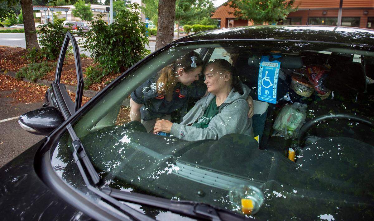 Carol Hampton gets a hug from her dialysis caregiver Brandy Snyder as she waits in the parking lot July 3 for her four-hour, thrice-weekly treatments in Tumwater. “She goes for dialysis and has to sit for four hours,” Arnold said. “And then we come here to sleep in a car where she can’t stretch out. Homeless is hard.”