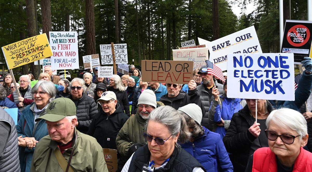 About 100 people opposed to the Trump administration gathered Tuesday morning outside the Lacey City Hall-based offices of Congresswoman Marilyn Strickland to urge her to stand up to Trump’s actions.