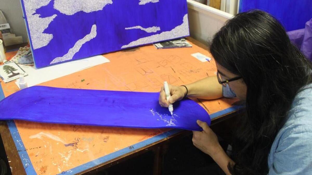 Olympia artist Jean Nagai creates art on a skateboard deck for “Decked Out” at the Pacific Bonsai Museum. The deck will look similar to the painting in the background.