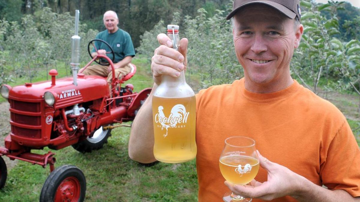 
Rich Cockrell displays his hard cider in his 17-acre Puyallup apple orchard last fall. Friend and helper Ron Book sits on the tractor he helped Cockrell restore. “I think as people’s taste and knowledge in cider grow, they’re learning to appreciate it more,” Cockrell said recently.
