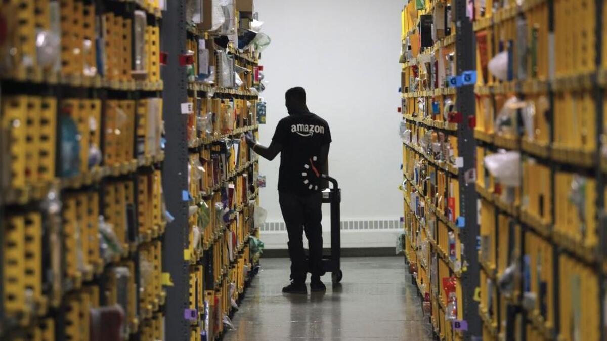 An employee of Amazon PrimeNow stacks shelves for customers making last-minute holiday orders at a distribution hub in New York in 2016. Amazon announced Tuesday that it would raise its hourly minimum wage to $15. Those who already made $15 will get an extra dollar an hour when the change is made next month, but they will also lose two benefits they relied on: monthly bonuses that could top hundreds of dollars and a chance to own Amazon’s sky-rocketing stock, currently worth nearly $2,000.